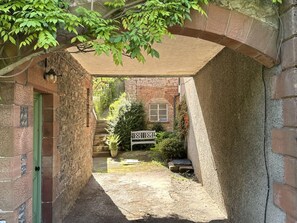 Ein Gebäude aus Stein mit einem überdachten Gang, einer grünen Tür und einer Bank im Hintergrund.