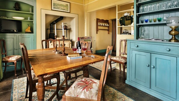 A dining room with a wooden table, chairs, and a blue cabinet with glassware. - Cottage in Heart of the Eden Valley (Penrith)