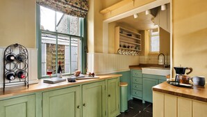 A kitchen with green cabinets, a window with floral curtains, and a coffee maker on the counter. - Cottage in Heart of the Eden Valley (Penrith)