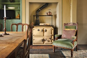 Une pièce au décor traditionnel, avec une table à manger en bois, un fauteuil à revêtement vert et un meuble d’époque doté de nombreux tiroirs.