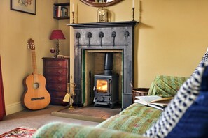 Ein gemütliches Wohnzimmer mit Kamin, Gitarre, Lampe und Bücherregal.