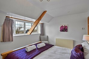 Ein Schlafzimmer mit schrägen Wänden, einem Bett mit violetter Bettdecke, einem grauen Sessel und einer Heizung.