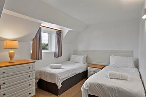 Un dormitorio con dos camas, una ventana con cortinas, una lámpara de noche y una mesita de noche de madera.