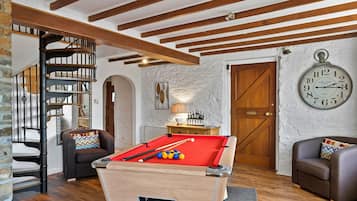 A cozy room with a pool table, a clock, and a bookshelf.