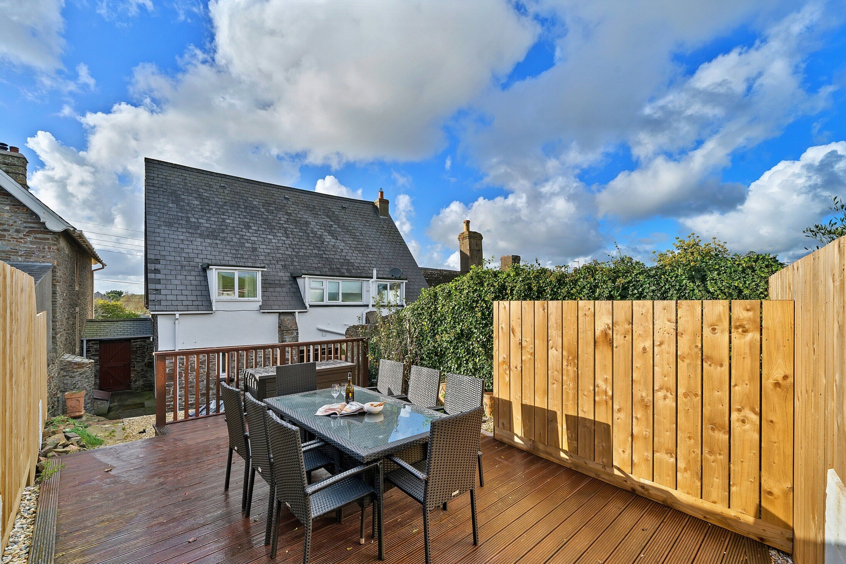 A patio with a table and chairs, a wooden fence, and a house with a grey roof in the background.