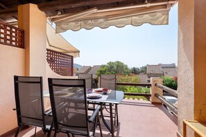 An outdoor patio with a table and chairs, a pergola overhead, and a view of buildings and greenery in the background. - Apartment 'Marea  - By and Service' (Golfo Aranci)