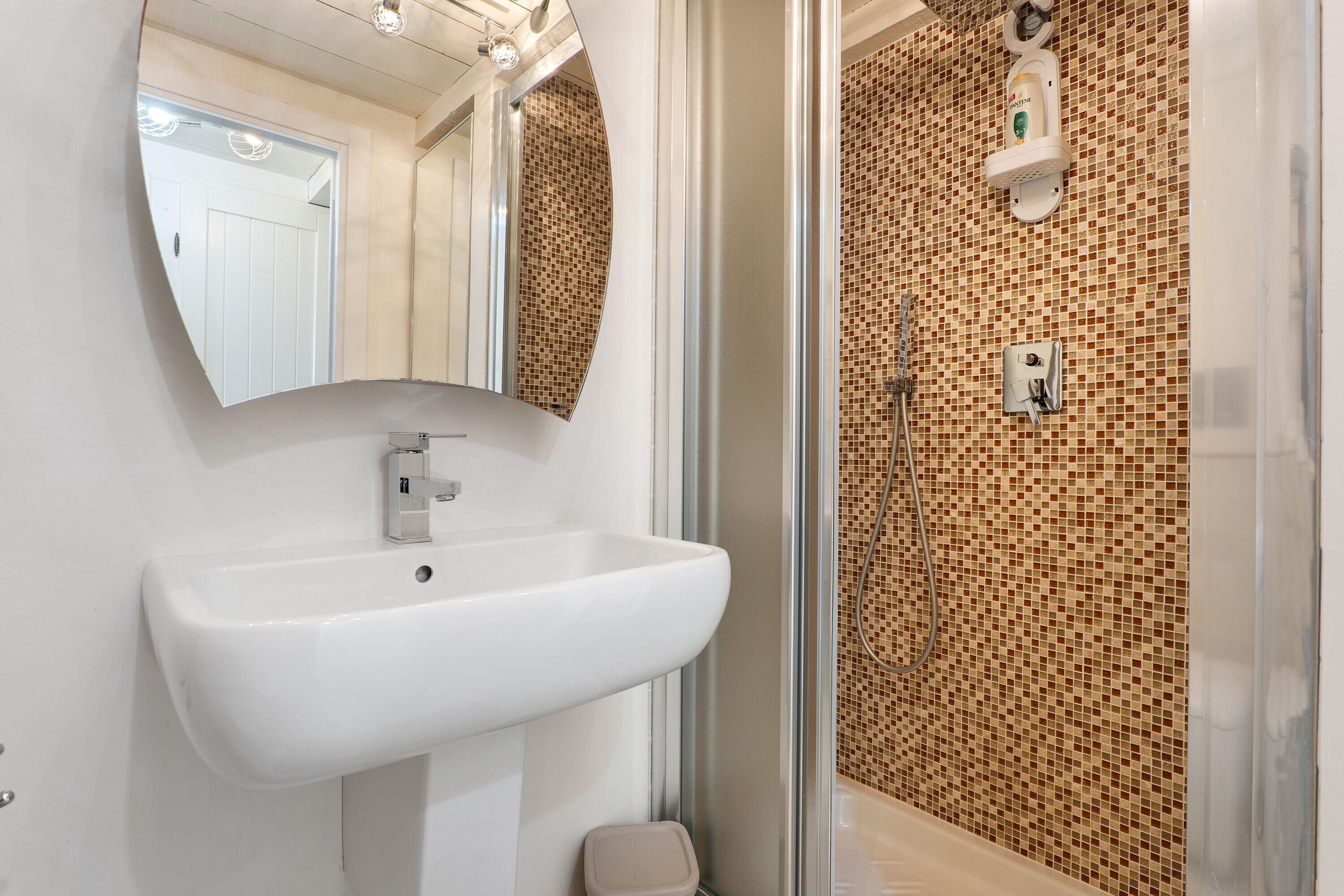 A bathroom with a white sink, a mirror, a shower with a tiled wall, and a handheld showerhead.