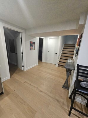 An interior space with a wooden floor, a staircase, a dining area with a table and chairs, and a door leading to another room. - Come Stay at "Night at the Movies" with all the comforts of home! (Calgary)