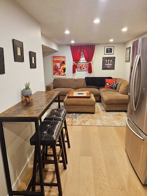 A modern living room with a dining area, a sofa set, a coffee table, and a refrigerator. - Come Stay at "Night at the Movies" with all the comforts of home! (Calgary)