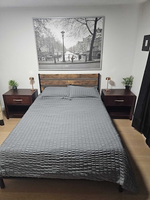 A bedroom with a large bed, two nightstands, a wooden headboard, a wall-mounted painting, and two potted plants. - Come Stay at "Night at the Movies" with all the comforts of home! (Calgary)