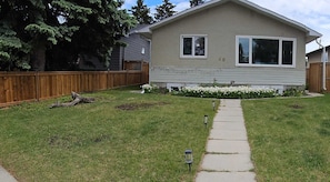 A two-story house with a visible number '20' on the side, a wooden fence, a well-maintained lawn, and a pathway leading to the front door. - Come Stay at "Night at the Movies" with all the comforts of home! (Calgary)