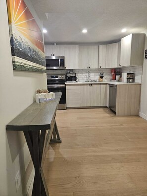 A modern kitchen with white cabinets, a microwave, a coffee machine, and a wooden dining table. - Come Stay at "Night at the Movies" with all the comforts of home! (Calgary)