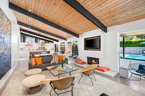 A modern living room with a fireplace, a dining area, and a kitchen. - Historic Midcentury Home w/ Pool and Hot Tub (Palm Springs)