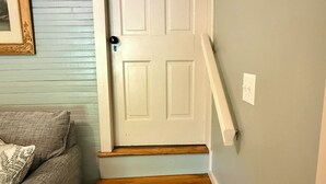 A staircase with wooden steps leading to a white door, a gray couch, and a wall-mounted light fixture. -  1-bedroom cottage in charming Meadowview established in 1908 (Meadowview)