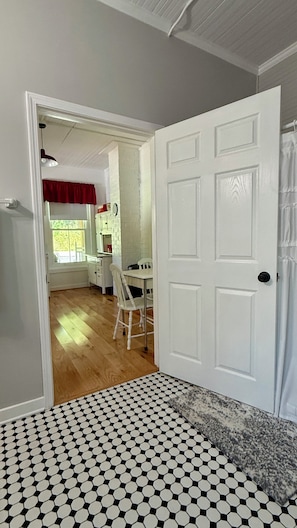 A room with a patterned floor, a white door, and a view into a kitchen area with a dining table and chairs.