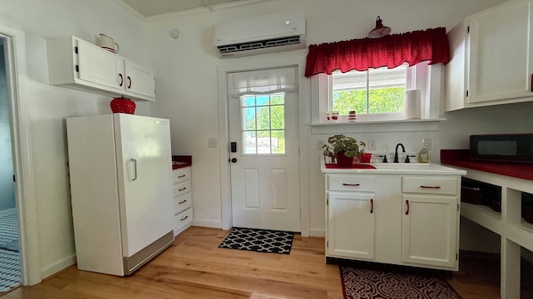 A compact kitchen with a refrigerator, a sink, and a window with a view of greenery.