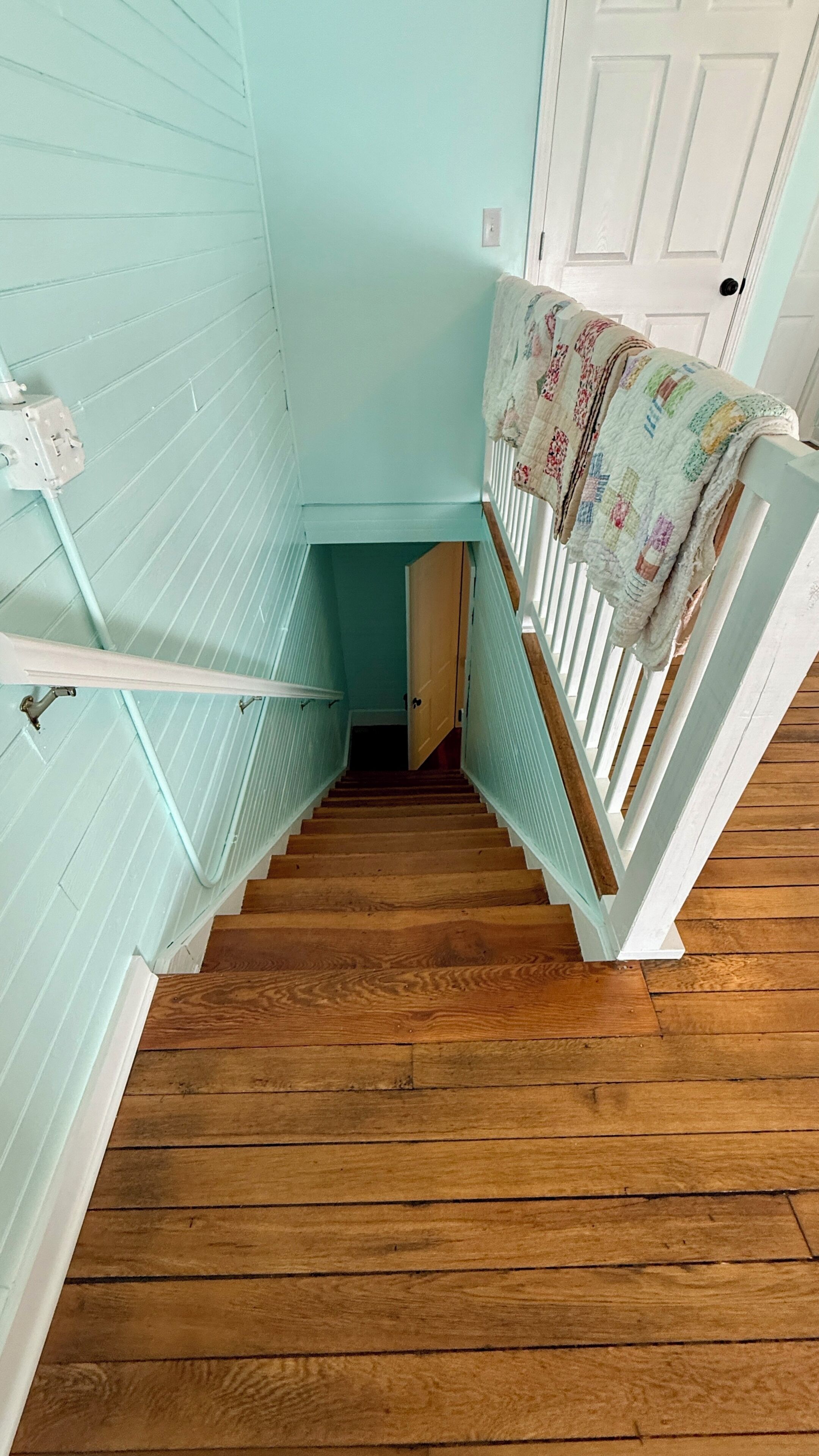 A wooden staircase with a white railing, leading to a door with a quilted blanket draped over it.