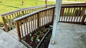 Eine Holzterrasse mit Geländer, einem Betonboden und einem Blumenbeet mit verschiedenen Blumen.
