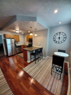 A modern kitchen with wooden cabinets, a stainless steel refrigerator, and a dining area with a round table and chairs. - Spacious 2BR South Side Retreat | Free Parking | Fast WiFi (Pittsburgh)