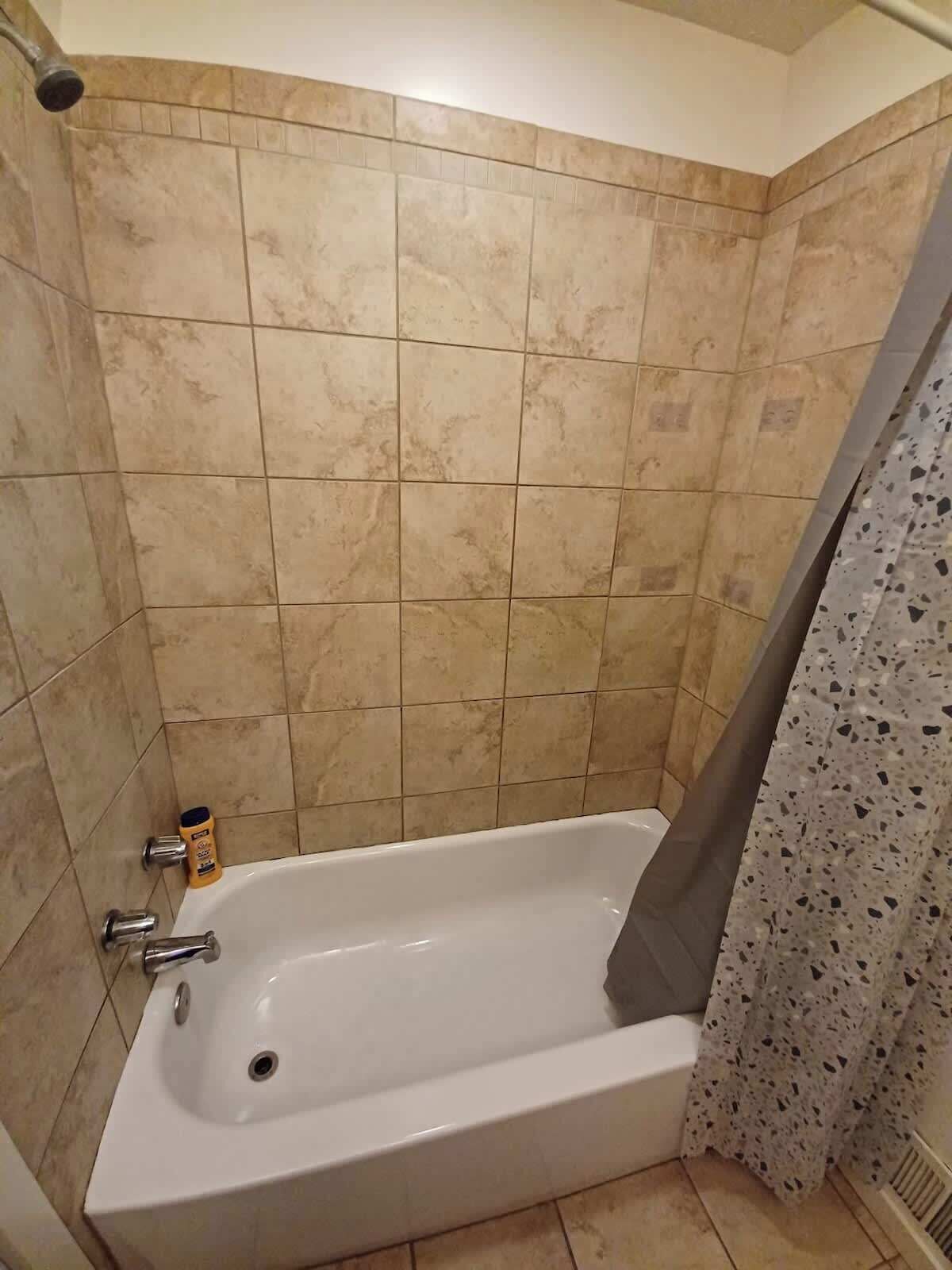 Ein Badezimmer mit einer Badewanne, einer Duschvorhang und einer Shampooflasche auf dem Boden.