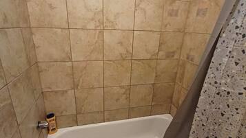Ein Badezimmer mit einer Badewanne, einer Duschvorhang und einer Shampooflasche auf dem Boden.