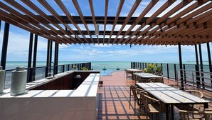 Una terraza exterior con una pérgola de madera, una barra y mesas con sillas.