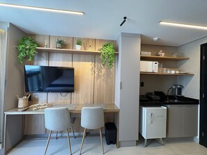 Una cocina moderna con televisión integrada, armarios de madera, un refrigerador pequeño y dos sillas junto a una mesa de comedor.