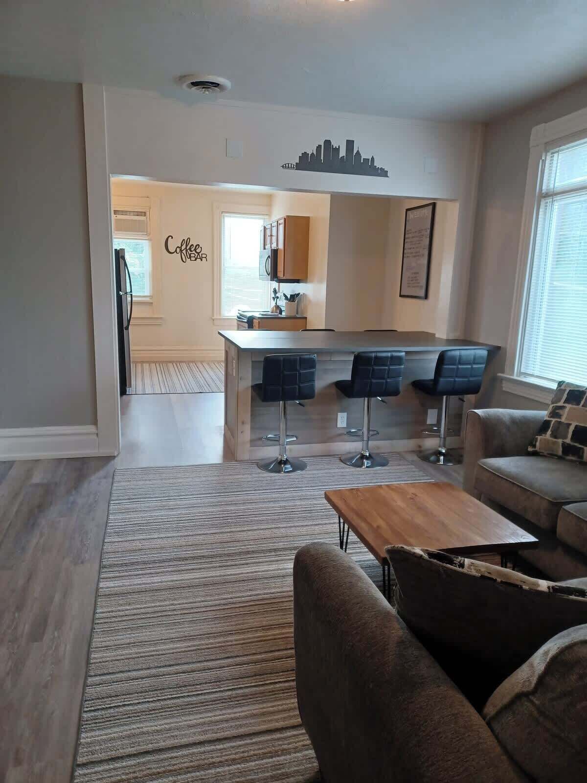 A modern living room with a sofa, a coffee bar, and a kitchen area with bar stools.