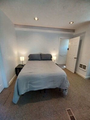 Een hotelkamer met een bed, twee bedlampen, een deur en een vloerbedekking.