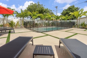 A pool area with two lounge chairs, a red umbrella, and a fenced pool. - Heated Pool 4BR Sleeps 12 · 6 Min to Dania Beach (Dania Beach)
