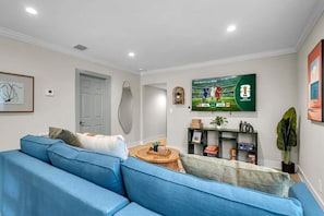 A living room with a blue sofa, a television displaying the FIFA World Cup, and a door in the background. - Heated Pool 4BR Sleeps 12 · 6 Min to Dania Beach (Dania Beach)