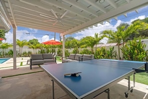 An outdoor ping pong table with a ceiling fan, surrounded by outdoor seating and palm trees. - Heated Pool 4BR Sleeps 12 · 6 Min to Dania Beach (Dania Beach)