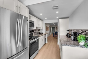 A modern kitchen with stainless steel appliances, a tiled backsplash, and a wooden floor. - Heated Pool 4BR Sleeps 12 · 6 Min to Dania Beach (Dania Beach)