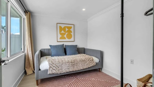 Een slaapkamer met een bed, een raam met gordijnen, een lijst met abstract kunstwerk en een kamerbreed tapijt.