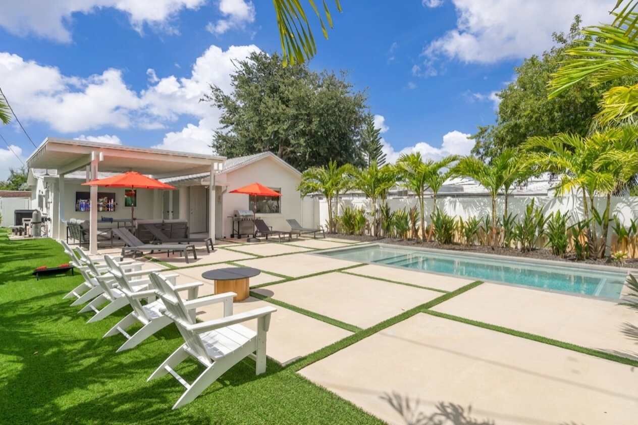 A backyard with a swimming pool, lounge chairs, and umbrellas.