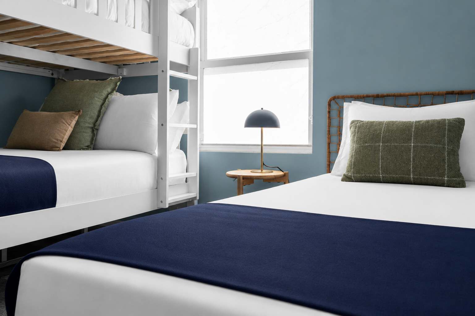 A bedroom with bunk beds, a bedside table with a lamp, and a window with blinds.