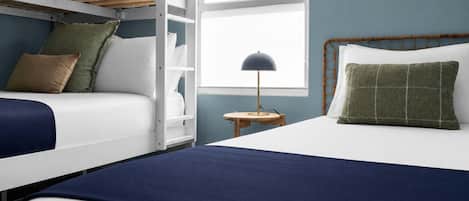A bedroom with bunk beds, a bedside table with a lamp, and a window with blinds.