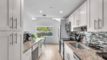 A modern kitchen with white cabinetry, granite countertops, and a view of greenery outside.