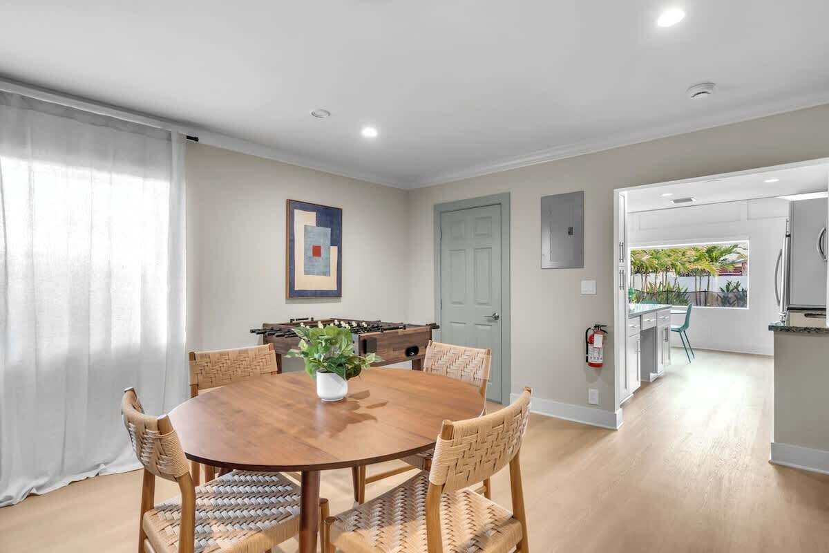 A dining area with a round wooden table, woven chairs, and a potted plant.