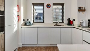 A modern kitchen with white cabinetry, a built-in oven, a sink, and a window with blinds. - Stunning Broad Haven Beach House (Haverfordwest)