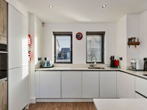 A modern kitchen with white cabinetry, a built-in oven, a sink, and a window with blinds. - Stunning Broad Haven Beach House (Haverfordwest)