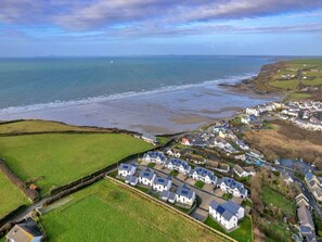 An aerial view of a coastal residential area with houses, a beach, and a view of the sea. - Stunning Broad Haven Beach House (Haverfordwest)