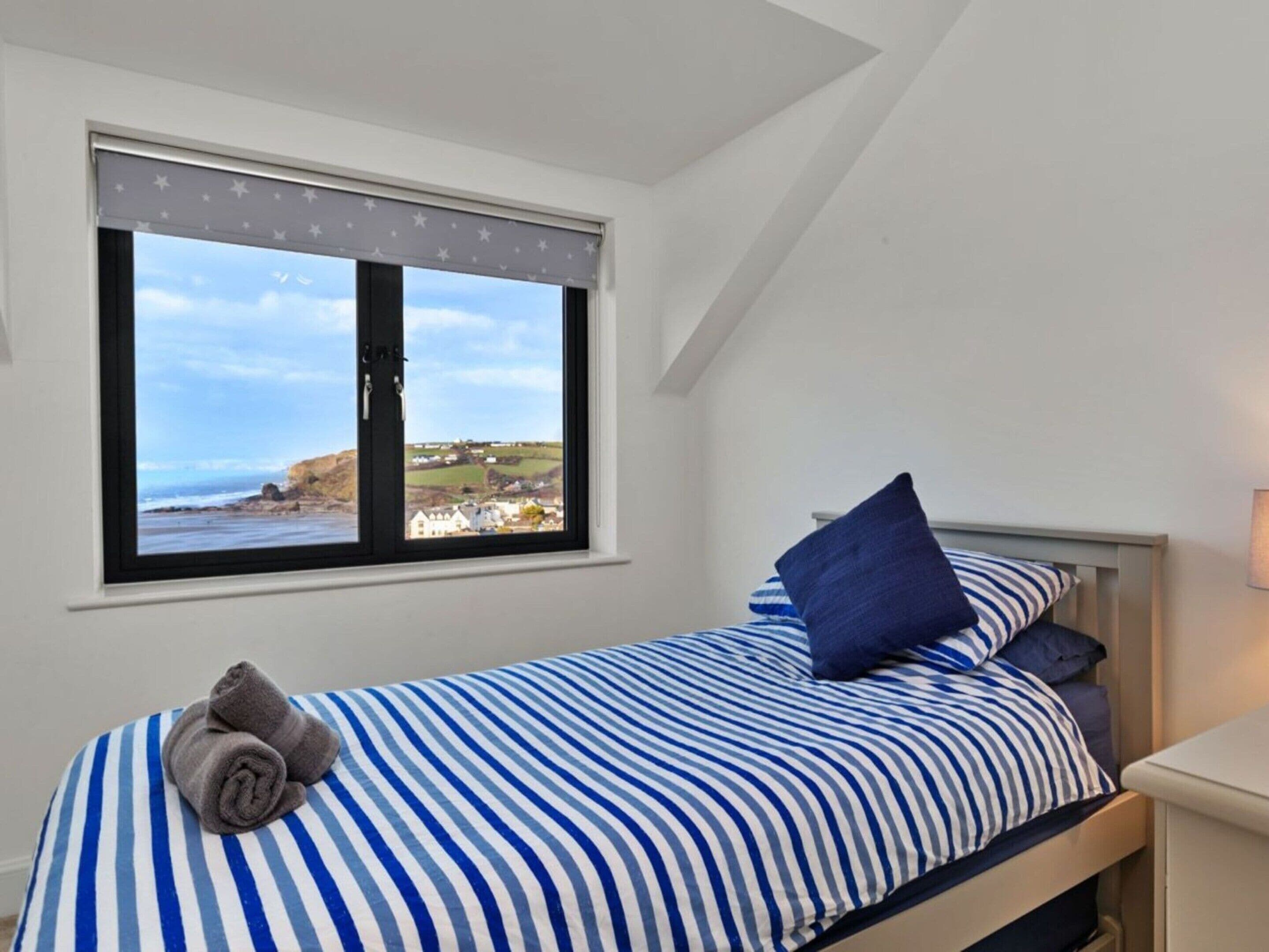 A bedroom with a bed, a window with a view of the coast, and a towel on the bed.
