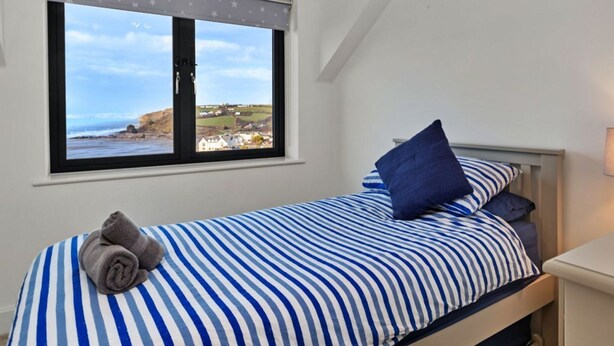 A bedroom with a bed, a window with a view of the coast, and a towel on the bed. - Stunning Broad Haven Beach House (Haverfordwest)
