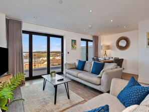 Una sala de estar moderna con un sofá, una mesa de centro y un televisor. Hay un balcón con vistas al campo.