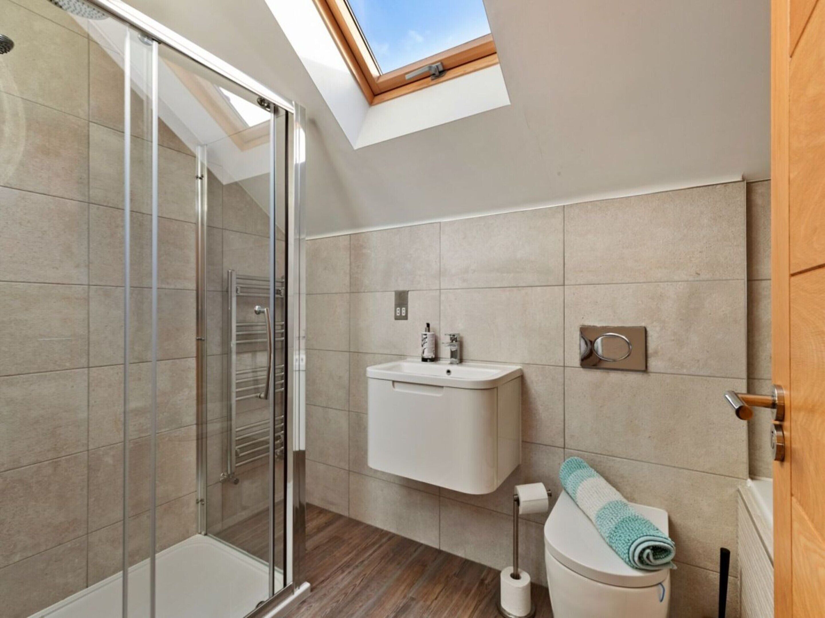 A modern bathroom with a skylight, a glass shower enclosure, a toilet, and a sink.