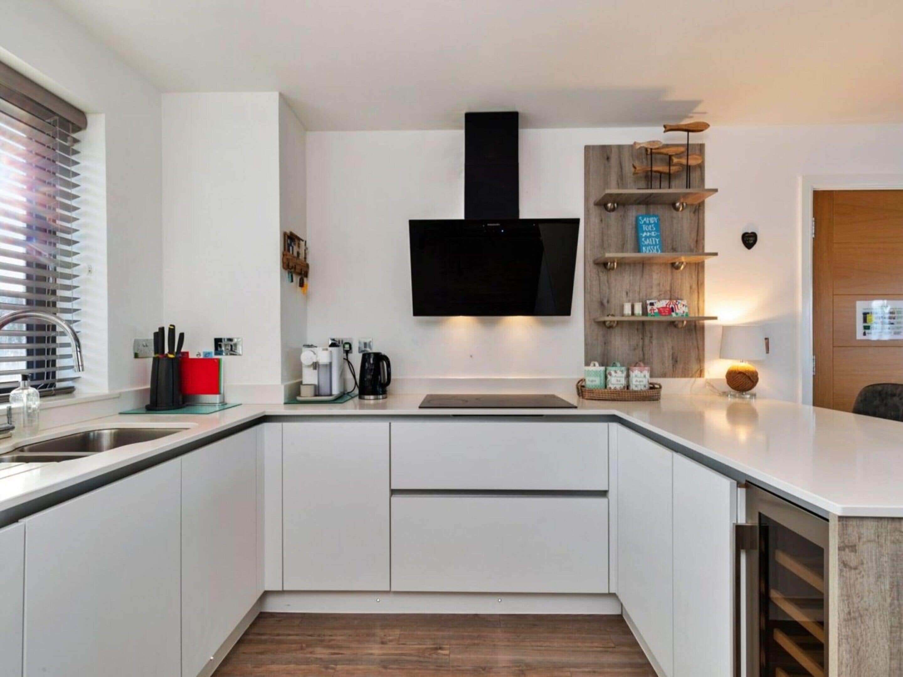 A modern kitchen with white cabinetry, a built-in stove, a coffee maker, and a flat-screen TV mounted above the stove.
