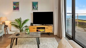 A modern living room with a flat-screen TV, a coffee table, a sofa, and a large window offering a view of the sea. - Stunning Broad Haven Beach House (Haverfordwest)