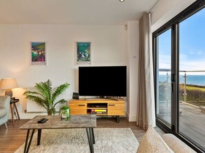 A modern living room with a flat-screen TV, a coffee table, a sofa, and a large window offering a view of the sea. - Stunning Broad Haven Beach House (Haverfordwest)