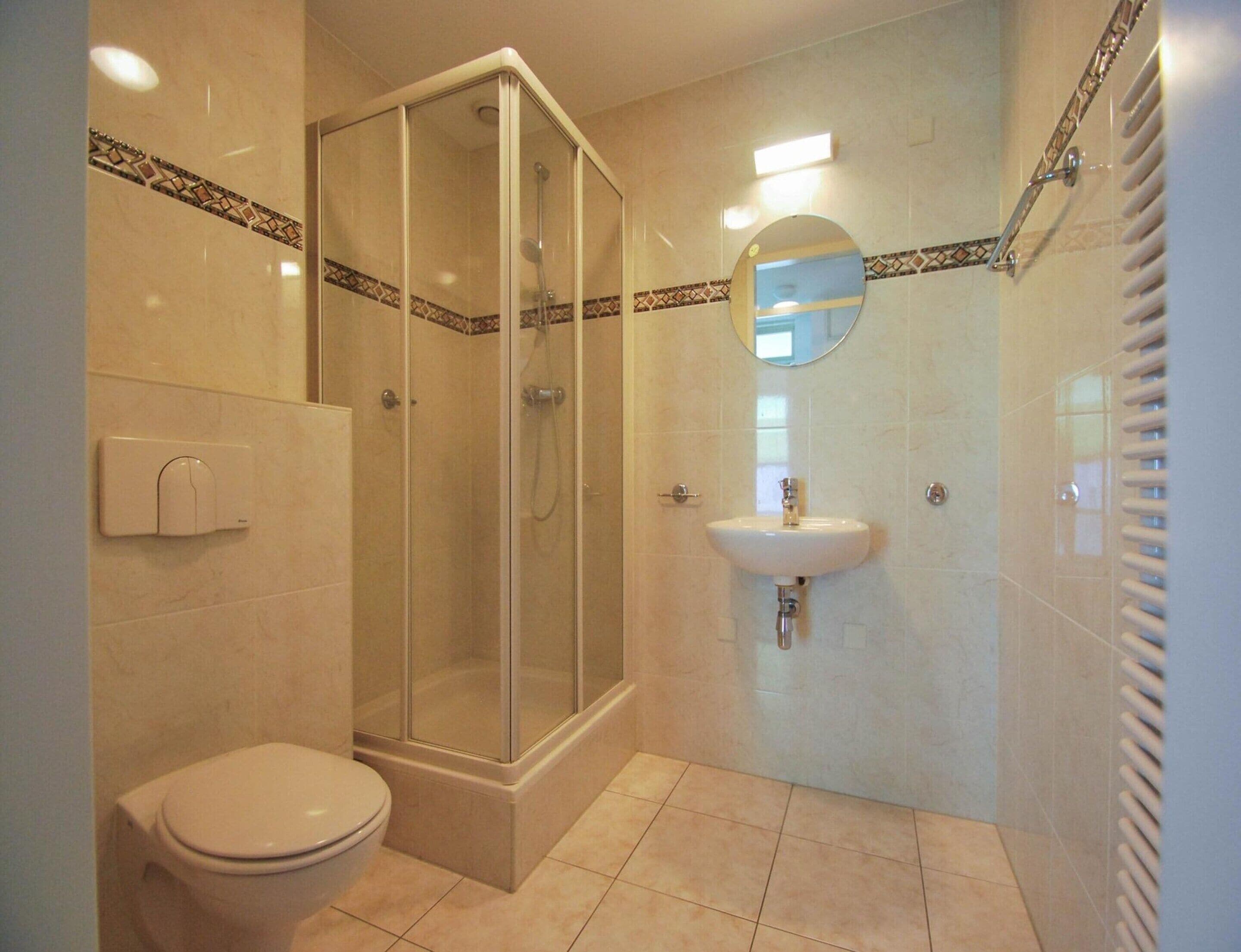 Een badkamer met een glazen douchecabine, een wit toilet, een wastafel met spiegel erboven en een handdoekhouder.